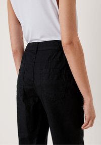 Pantalons en lin noir à taille haute, dotés de deux poches arrière et de détails de couture. Le tissu a une finition légèrement texturée.