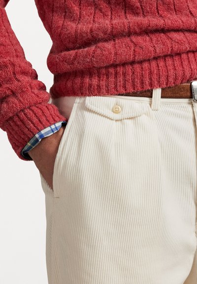 Jersey rojo de punto con textura acanalada; combinado con pantalones de pana en color crema que cuentan con un bolsillo abotonado y los puños de una camisa de cuadros metidos.