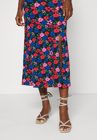Květinová midi sukně s černým pozadím, zdobená živými růžovými, červenými a modrými květinami, s bočním rozparkem. V kombinaci se světle šedými sandály na pásky.