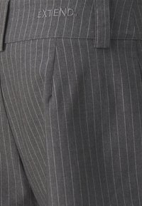 Šedé pruhované kalhoty vyrobené z texturované tkaniny, s nažehlenými záhyby a vyšitým logem "EXTEND" na pase.