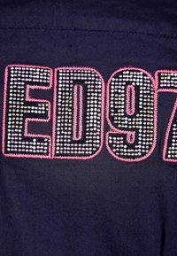 Tessuto blu navy con grande design "ED97" composto da strass argento e rosa, con un ricamo a contrasto che contorna le lettere.