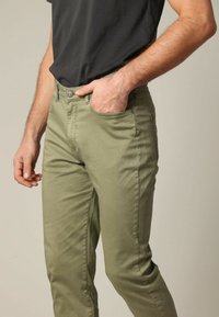 Pantalons en coton stretch vert olive avec une coupe ajustée, comprenant une poche avant, une fermeture éclair et un bouton. Texture lisse, détails minimalistes.
