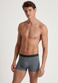 Men’s boxer briefs with a dark gray base, featuring a green and yellow star pattern, elastic waistband with black and green detailing.