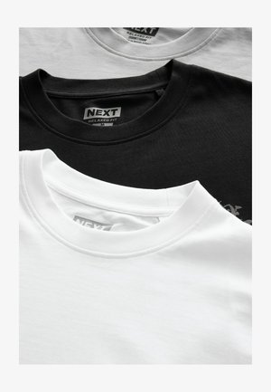 Trois t-shirts empilés : un blanc, un gris, un noir. Chacun a un col rond et une étiquette de coupe décontractée à l'intérieur. Texture en coton.