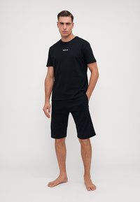 Camiseta negra de manga corta con el logo "REPLAY", combinada con pantalones cortos negros de longitud a la rodilla. Material de algodón, corte relajado, diseño minimalista.