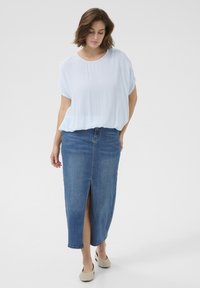 Blouse bleu clair, ample, avec un décolleté rond, associée à une jupe en denim bleu foncé, longueur genou, avec une fente à l'avant.