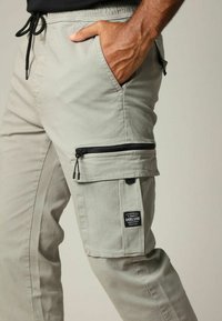 Lichtgrijze cargobroek met een ontspannen pasvorm, voorzien van een ritssluiting zak, zijzakken, een koordsize en een textuurstof.