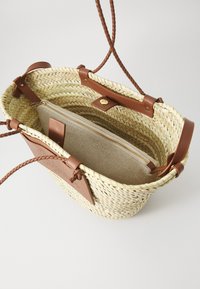 Πλεκτή τσάντα από άχυρο με καφέ δερμάτινες λεπτομέρειες, διαθέτοντας πλεγμένες λαβές και μια τσέπη από ύφασμα με φερμουάρ στο εσωτερικό για οργάνωση.