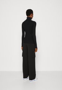 Zwarte geribbelde coltrui gecombineerd met losse zwarte cargobroeken. De outfit heeft lange mouwen en cargozakken op de broek.