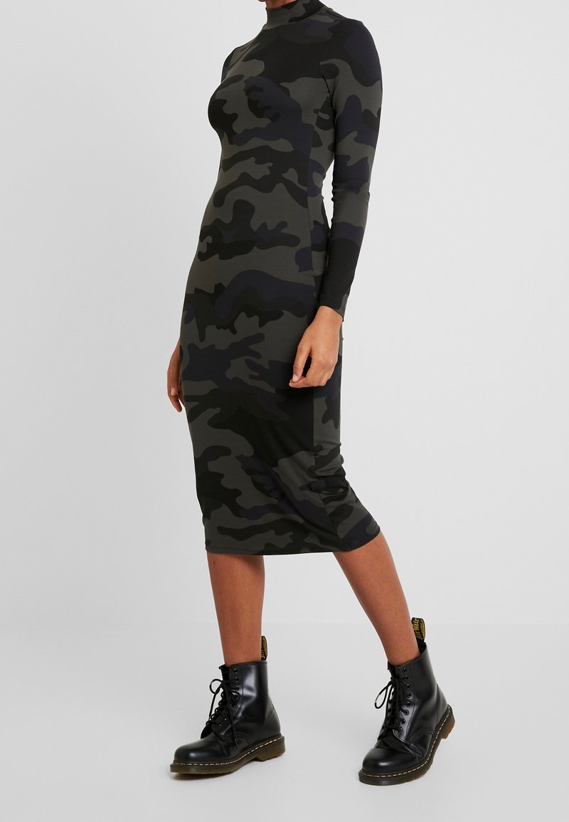 Kamo-mönstrad, figursydd klänning med långa ärmar, hög hals och knä-lång fåll. Bärs med svarta snörkängor för extra kontrast.