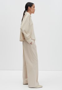 Beige blouse met lange mouwen en een losse pasvorm, gecombineerd met beige wijde broek. Gladde stof met minimale accenten en zakken.