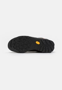 Suola di scarpa in gomma nera con scanalature profonde per una migliore aderenza, caratterizzata da un logo Vibram giallo e un motivo circolare testurizzato per una presa ottimale.