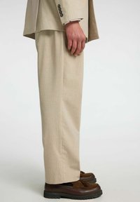 Beżowe spodnie garniturowe w prążki wykonane z lekkiego materiału. Projekt charakteryzuje się prostym krojem i jest zestawiony z ciemnobrązowymi mokasynami.