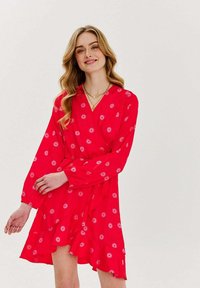 Červené zavinovací šaty s dlouhými rukávy, zdobené květinovým vzorem v světle růžové barvě. Sukně má volánkový lem a přiléhavý pas.