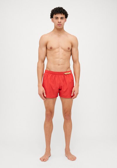 Shorts de bain rouges avec taille élastique présentant un détail de logo, fabriqués en tissu léger, longueur au-dessus du genou, et texture lisse.