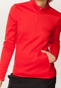 Suéter rojo con cuello de cremallera hecho de un tejido ligero y suave. Cuenta con mangas largas y bolsillos laterales con cremalleras, diseñado para la ropa deportiva.