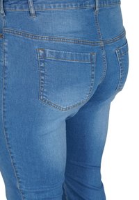 Vaqueros de mezclilla azul con un diseño ajustado. Las características incluyen dos bolsillos traseros, costuras claras y una textura suave.
