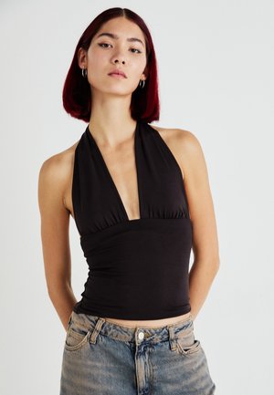 Haut halter noir avec un décolleté en V profond, tissu froncé au niveau de la poitrine et silhouette ajustée, associé à un jean en denim délavé.