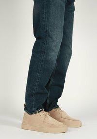 Sneaker in suede beige con un design a profilo basso, con punta arrotondata e suola in gomma beige, abbinate a jeans denim blu scuro.