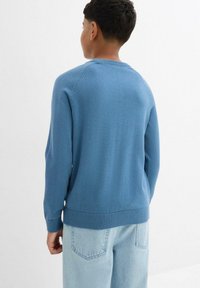 Maglione azzurro a maglia con collo rotondo, polsini e orlo a costine. Texture liscia e design semplice. Abbinato a jeans in denim azzurro chiaro.