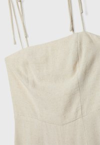 Robe en lin avec un corsage ajusté, de couleur crème, et des bretelles réglables à nouer. La texture est légèrement texturée avec une finition naturelle.