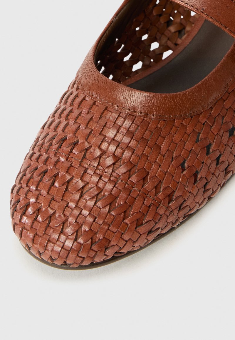Des chaussures en cuir marron présentant un design tissé, avec une semelle plate et un bout rond. La texture est lisse, avec une finition mate.