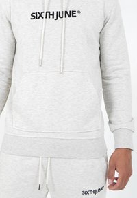 Sudadera gris claro con el logo negro "SIXTH JUNE", capucha con cordón, bolsillo frontal, puños y dobladillo acanalados, fabricada en un tejido suave.