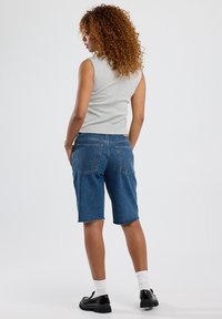 Mid-blue denim shorts with raw hem, four pockets, and stitching accents, paired with a light gray sleeveless top.