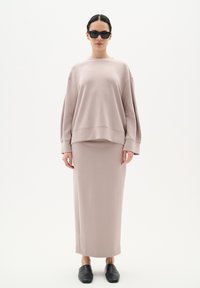 Ljusrosa, oversized sweatshirt i kombination med en matchande midi-kjol; slät textur, lös passform och svarta slip-on skor fulländar looken.