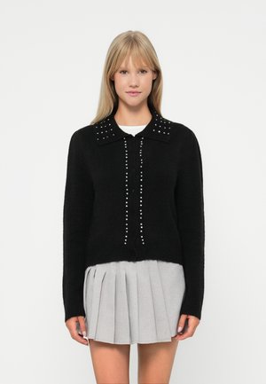 Gilet noir en tissu texturé, doté d'un col, d'une patte de boutonnage et de clous décoratifs le long de la patte et du col.