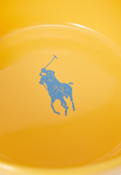 Dzeltena bļoda ar zilu polo spēlētāja logo centrā. Gluda tekstūra ar izliektiem malām un spīdīgu apdari.