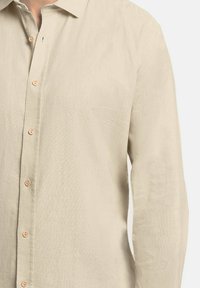 Camisa de manga larga beige en un tejido texturizado, con un cuello clásico y un cierre de botones en la parte delantera con botones de color claro.