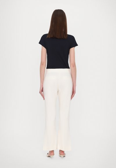 Marineblauwe top met korte mouwen gecombineerd met crème wijde broekspijpen, met een gladde textuur en een aangesloten tailleband, gezien vanuit de achterkant.