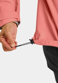 Light pink jacket with adjustable black drawstring at the hem, featuring a smooth fabric texture and a close-up of a hand gripping the cord.