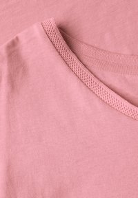 Ljusrosa bomullströjor med en mjuk textur, med en ribbad rund halsringning och överlappande tygsektioner.