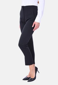 Pantaloni neri su misura con vita alta, design a gamba dritta e pieghe frontali. Abbinati a tacchi a punta neri e una camicia bianca.
