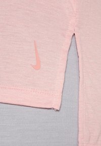 Camiseta rosa de Nike con mangas cortas, dobladillo recto, diseño ligeramente con aberturas laterales y un pequeño logotipo rosa en el dobladillo inferior.