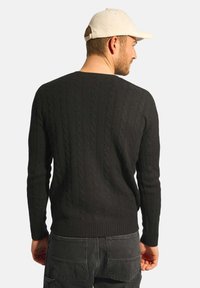 Czarny sweter w splot warkoczowy z okrągłym dekoltem i prążkowanym wykończeniem. Model ma na sobie ciemne spodnie i jasny kapelusz. Zaprezentowany widok z tyłu.