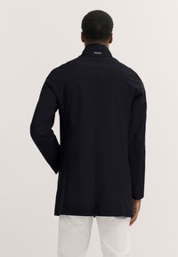 Schwarze wasserdichte Jacke mit steifem Kragen, langen Ärmeln und gerader Silhouette. Glatte Textur ohne sichtbare Beschläge.