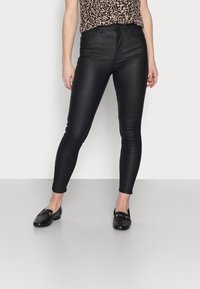 Černé faux kožené skinny džíny s hladkou texturou, vysokým pasem a přiléhavým střihem, zkombinované s černými mokasíny a vzorovaným topem.
