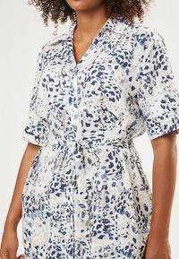 Kurzärmliges, knöpfbares Kleid aus leichtem Stoff mit einem abstrakten Muster in Blau und Creme. Inklusive eines Bindegürtels in der Taille.