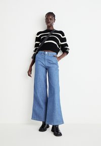 Zwart-wit gestreepte trui, losse blauwe wijde jeans en zwarte enkelboots. Denim heeft een zachte textuur; de trui is gebreid.