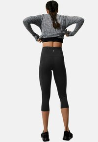 Grå langärmad träningsskjorta med texturerad väv, tillsammans med åtsittande svarta capribyxor med hög midja och bakfickdetalj.