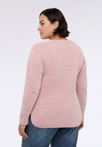 Rosa gestrickter Pullover mit strukturiertem, geripptem Muster, rundem Ausschnitt und langen Ärmeln; hat einen leicht verlängerten hinteren Saum und seitliche Schlitze.
