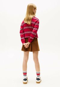 Rood gestreepte trui, bruine rok, witte sokken met rode en blauwe strepen, witte schoenen met een blauw accent. Het haar is steil en blond.