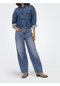 Korta denimjacka med knapprad fram och bröstficka, i kombination med högmidjade vida jeans. Båda i medelblå tvättad denim.