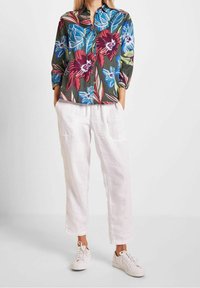 Camisa de botones con estampado floral en verde oscuro con flores en azul, rojo y blanco; combinada con pantalones de lino blancos y zapatillas blancas.