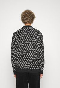 Pull noir avec un motif ondulé blanc, poignets et ourlet côtelés. Fabriqué en tissu doux, avec une coupe décontractée et un col rond.