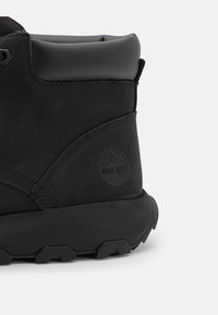 Stivale alla caviglia in suede nero con finitura testurizzata, dotato di suola in gomma e logo impresso. Il design include un collare imbottito per un supporto migliore.