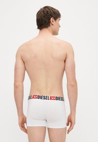 Balti bokseršorti ar melnu un sarkanu zīmolu jostu, pieguļoša fit un gluda tekstūra, redzami no mugurpuses.